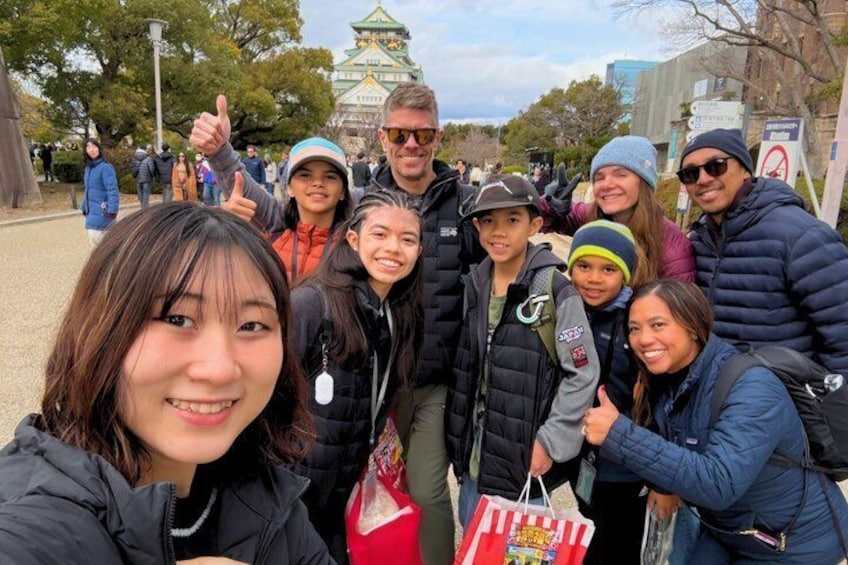 Un groupe de personnes se trouve dans un parc, avec un bâtiment traditionnel japonais en arrière-plan. 5