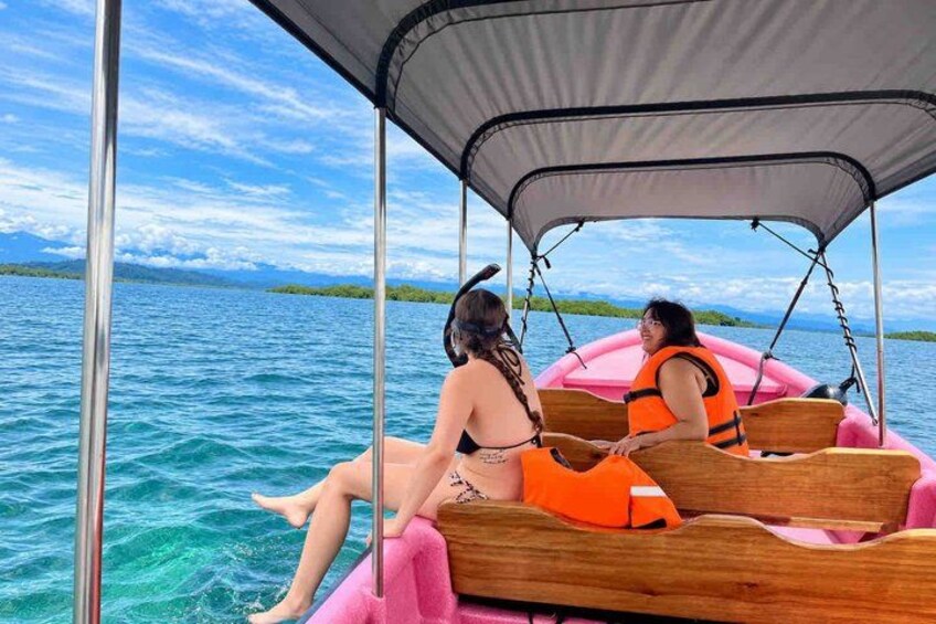 Two people on a boat with a canopy, sitting on wooden benches, surrounded by water and distant land. 1