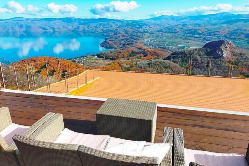 A wooden deck with wicker furniture overlooking a scenic landscape with a lake and autumn foliage. 1