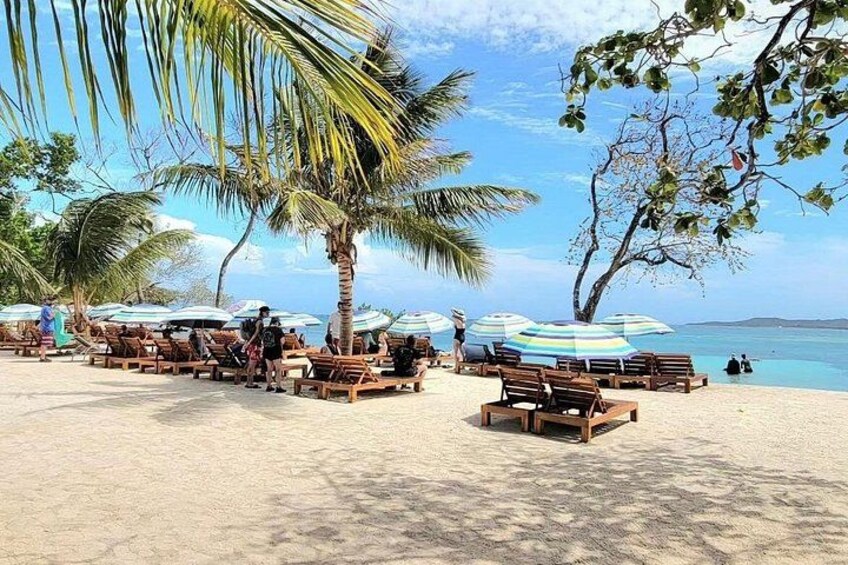 A beach with wooden lounge chairs and striped umbrellas. 1