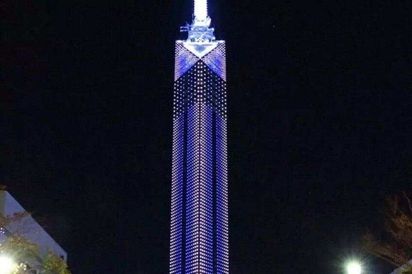 A tall building with a pointed top and a series of lights along its facade. 2