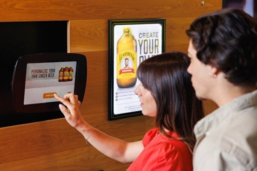 Eine Person bedient einen Touchscreen-Kiosk, im Hintergrund eine Anzeige für Ingwerbier. 4