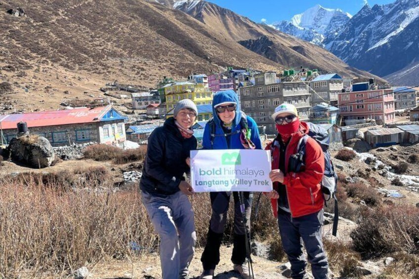 Three people standing on a mountain trail with a sign reading 'bold Himalaya Langtang Valley Trek.' 5