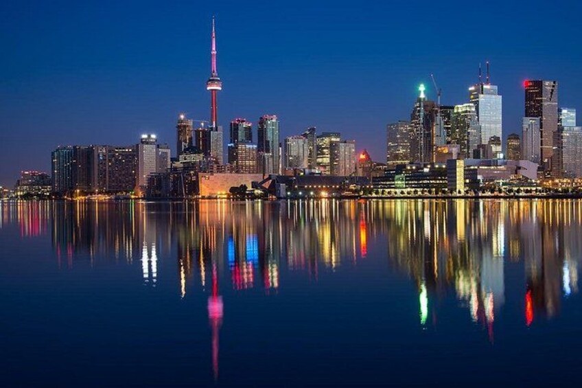 A city skyline at dusk with a prominent tower reflecting on the water. 2