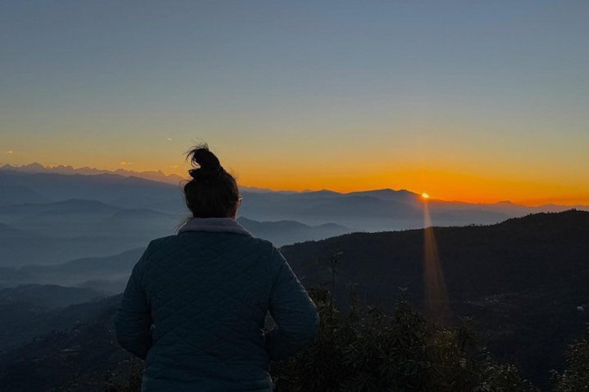 A person standing on a mountain overlooking a sunset with distant mountains in the background. 1