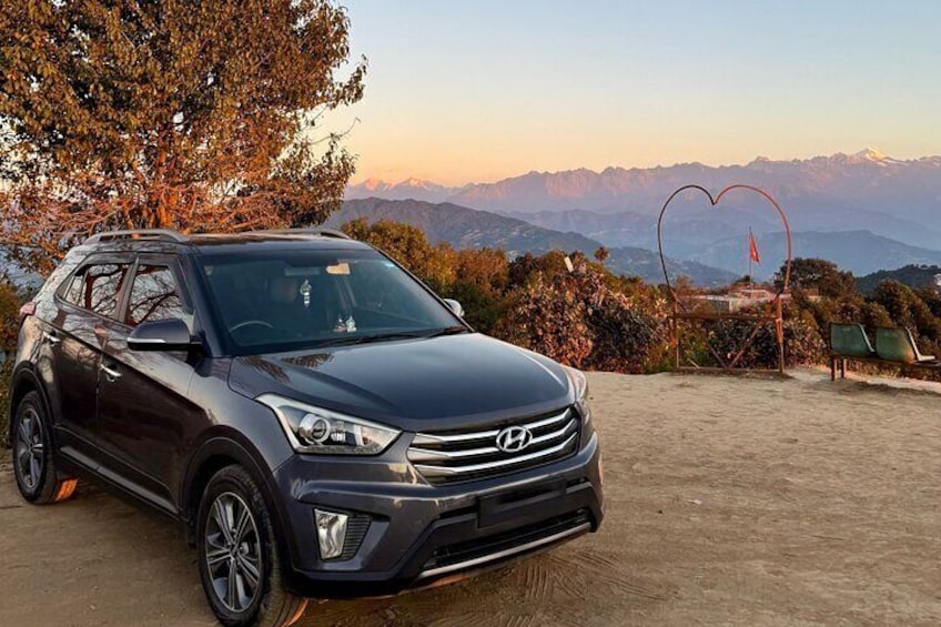 A dark-colored SUV parked on a dirt surface with a scenic mountain backdrop and a heart-shaped decoration. 4