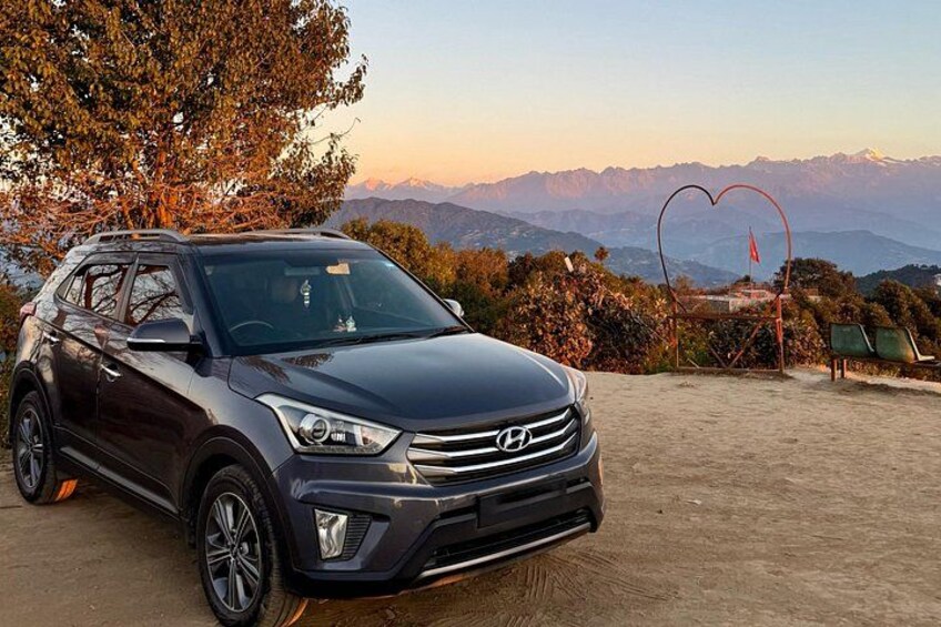 A dark-colored SUV parked on a dirt surface with a scenic mountain backdrop. 4