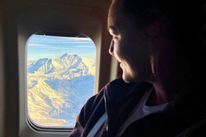 A person seated by an airplane window with a mountainous landscape visible outside. 1