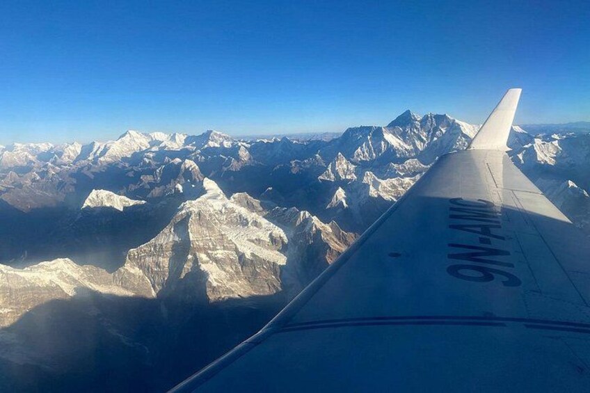 An airplane wing with the text '9N-ANX' and a mountainous landscape below. 2