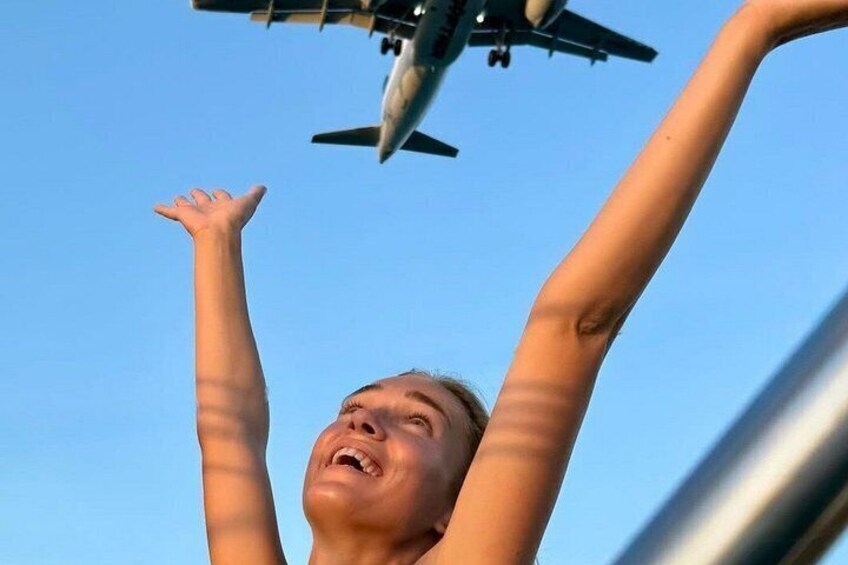 A person with arms raised, looking up at an airplane in the sky. 3