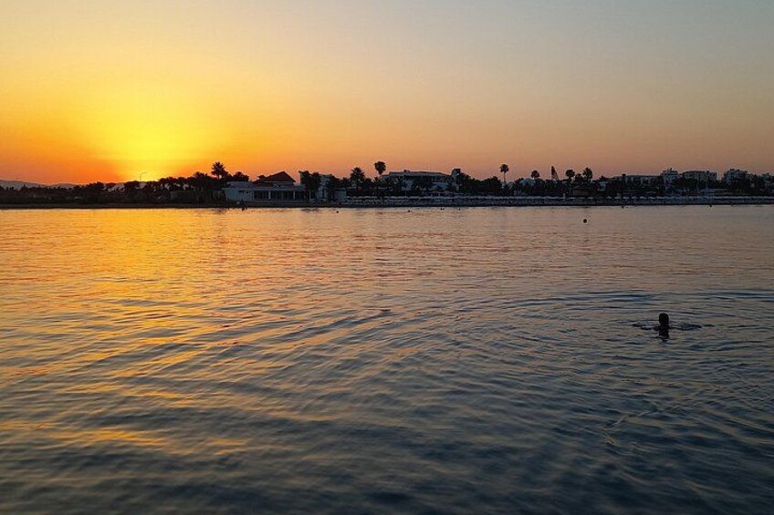 A sunset over a calm body of water with a silhouette of a person swimming in the foreground. 2