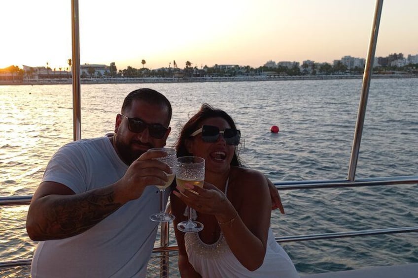 Two people toasting with champagne glasses on a boat with a sunset in the background. 2