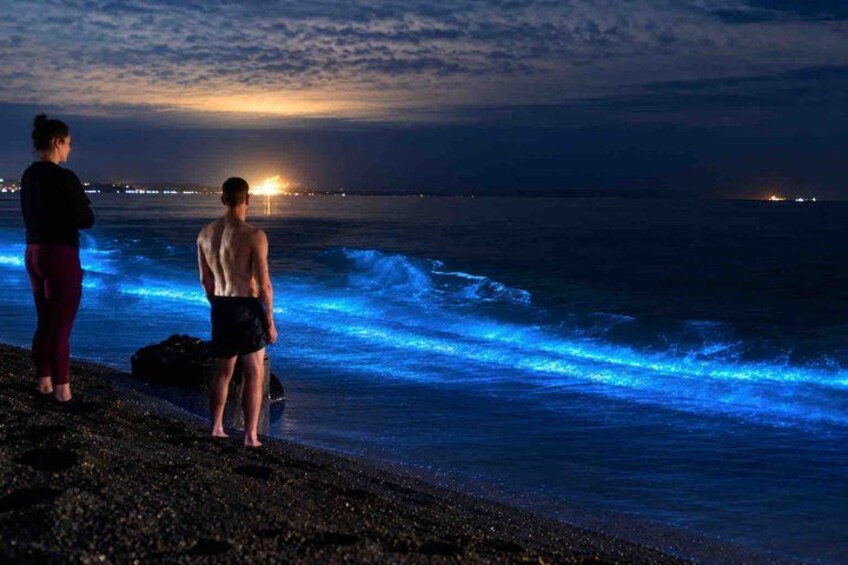 Two people standing on a rocky beach at sunset, with waves crashing onto the shore. 4