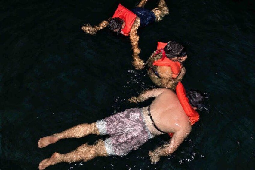 Two people swimming in a body of water, wearing life jackets. 3