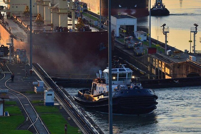 A large cargo ship docked at a port with industrial buildings and a tugboat nearby. 4
