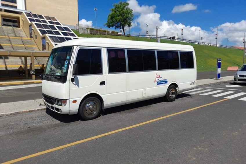 A white bus parked on a street with a pedestrian crossing and solar panels on a building in the background. 2