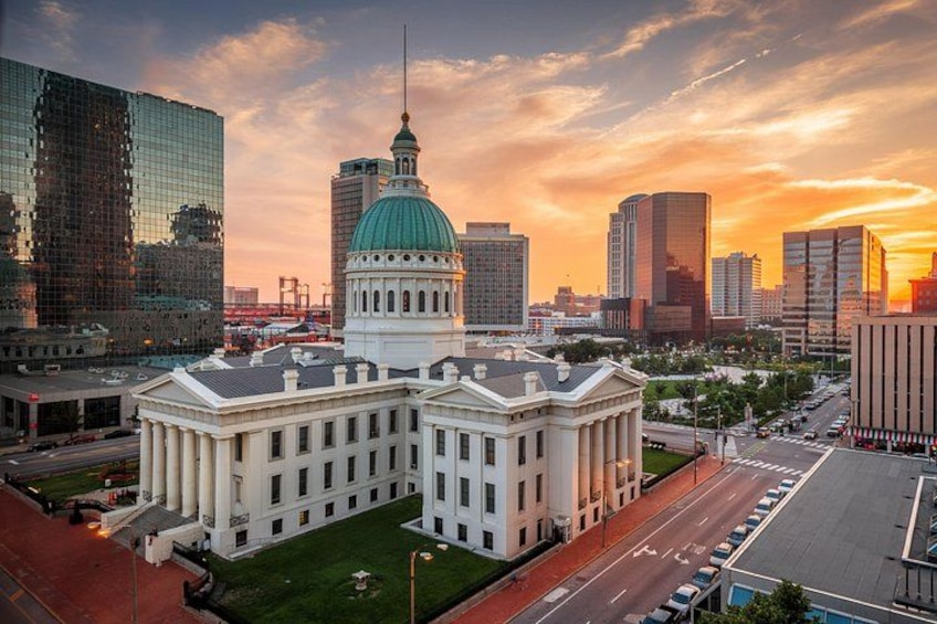 A cityscape with a prominent white building with a green dome, surrounded by modern skyscrapers and a sunset sky. 2