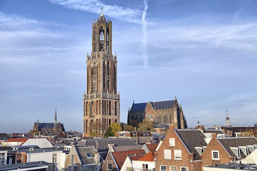 A tall Gothic-style church with a prominent tower, surrounded by residential buildings with red-tiled roofs. 1