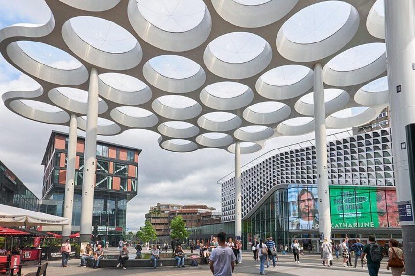 A modern urban square with circular canopies, a glass building, and a digital billboard. 4