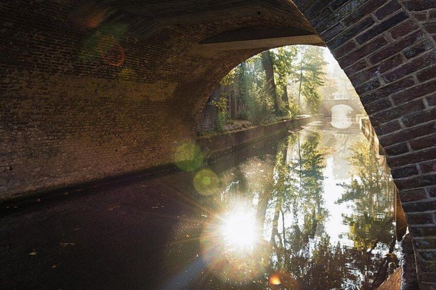 A bridge with a circular opening, sunlight reflecting off water, and trees in the background. 2