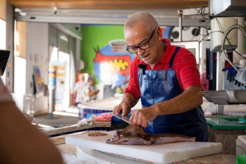 A person in a red shirt and blue apron cutting meat on a cutting board in a kitchen. 1
