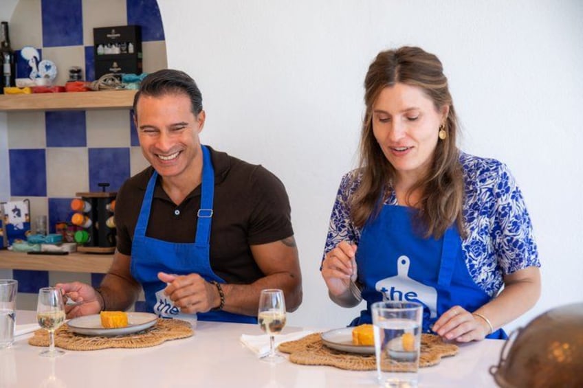 Dos personas con delantales sentadas a una mesa con platos de comida y copas de vino. 2