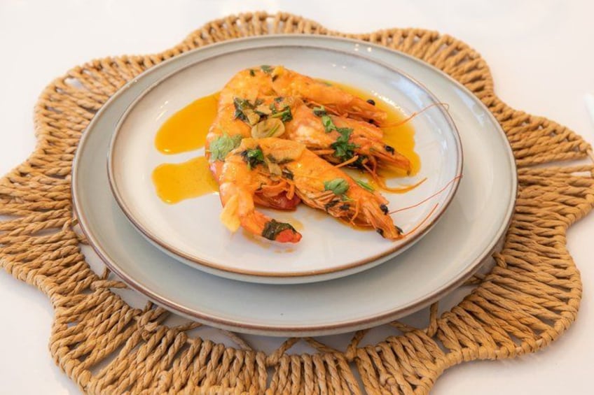 Un plato de camarones cocidos con salsa, adornado con hierbas, sobre una base de mimbre. 4