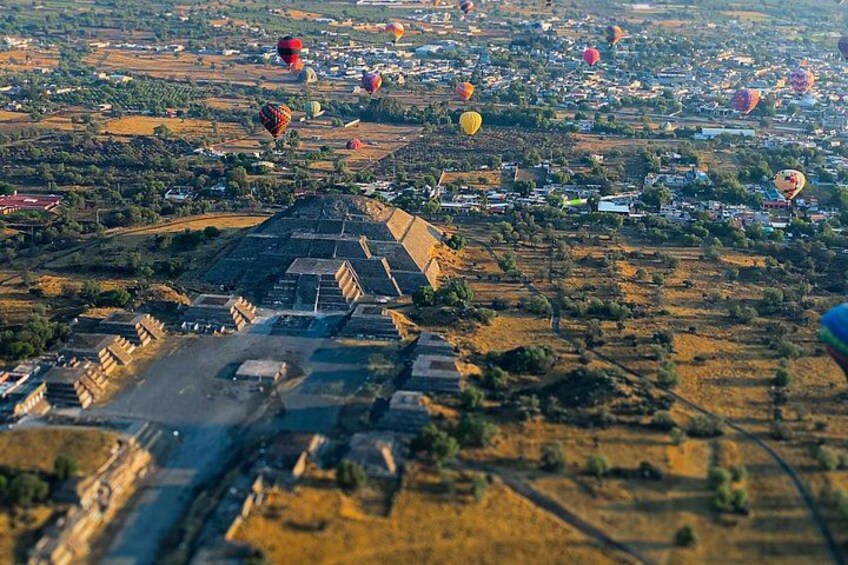 Un paisaje con varios globos aerostáticos, una estructura en forma de pirámide y una carretera. 3