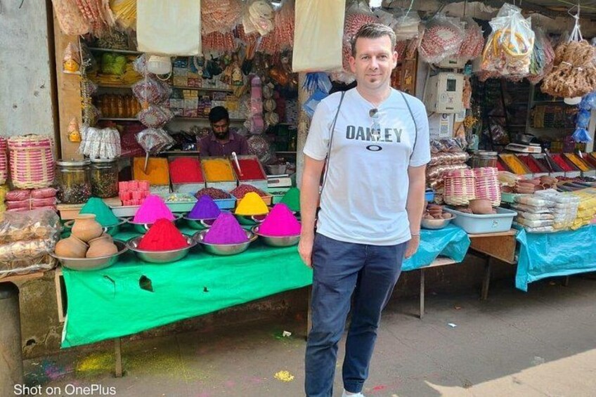 A man standing in front of a market stall with colorful powders and various packaged goods. 2