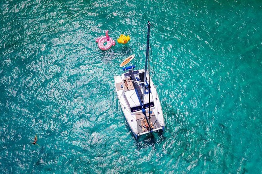 Een boot met een mast en een opblaasbaar, kleurrijk ringetje drijft op turquoise water. 5