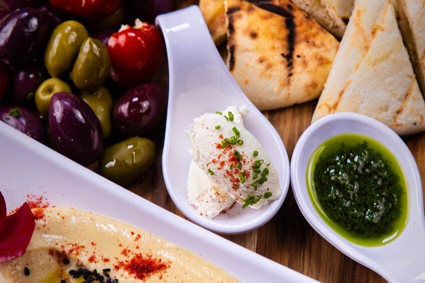 Ett urval av medelhavsrätter, inklusive oliver, hummus, pitabröd och en grön sås. 3