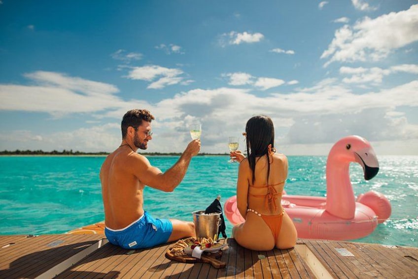 Een koppel op een houten terras aan zee, met een roze flamingo drijver. 3