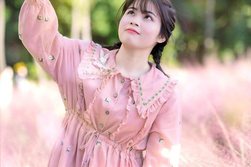 A person in a pink dress with ruffles and buttons, standing outdoors with trees in the background. 5
