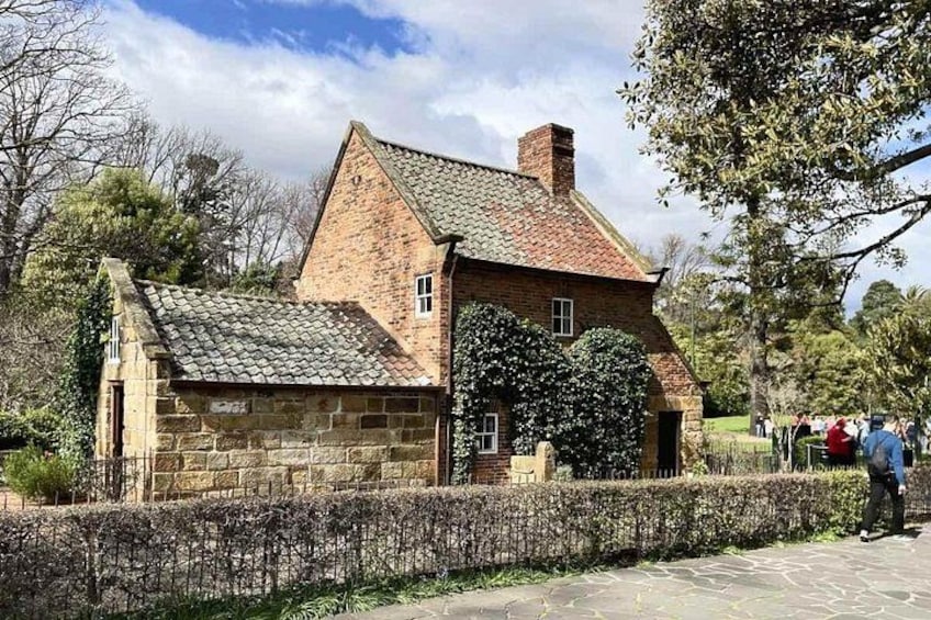 Une maison en pierre avec un toit en tuiles, entourée d’un mur de pierre et d’une haie. 1