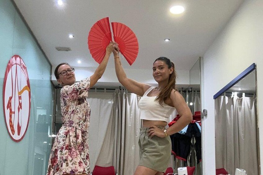 Two people holding a red fan in a room with a mirror and a red circular sign on the wall. 1