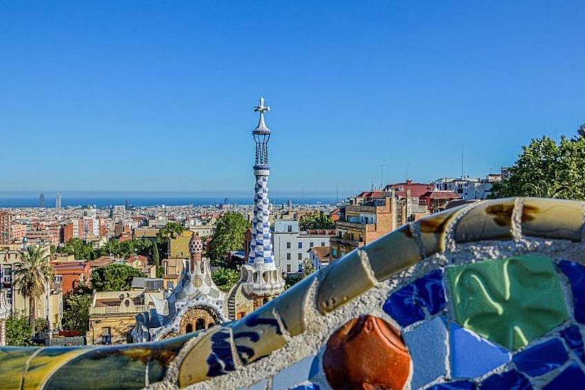 A tiled fence with mosaic patterns, a tower, and a cityscape with buildings and a clear sky. 2