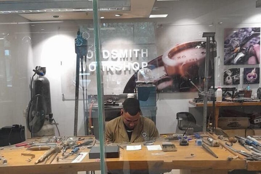 A workshop with tools and equipment, a man working at a desk, and a poster with the text 'DSMITH GIN SHOP' in the background. 2