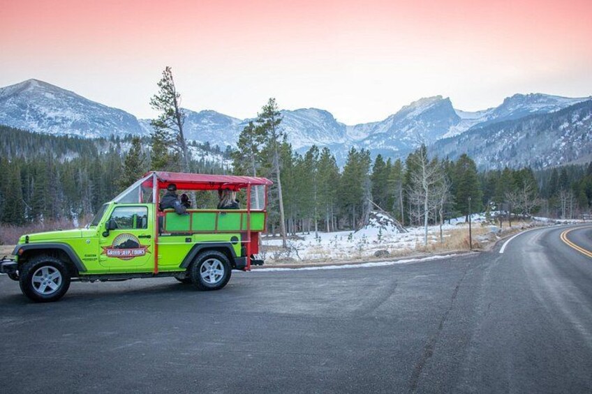 A green Jeep with a red roof parked on a road with snow-covered mountains in the background. 3