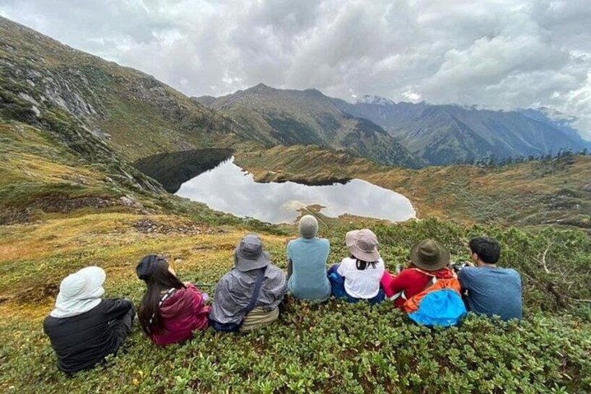 A group of people sitting on a grassy hill overlooking a lake with mountains in the background. 2