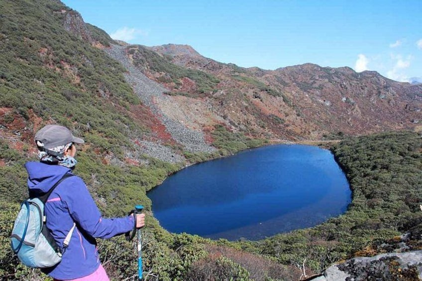 A hiker with a backpack and walking stick overlooking a lake surrounded by mountains. 4