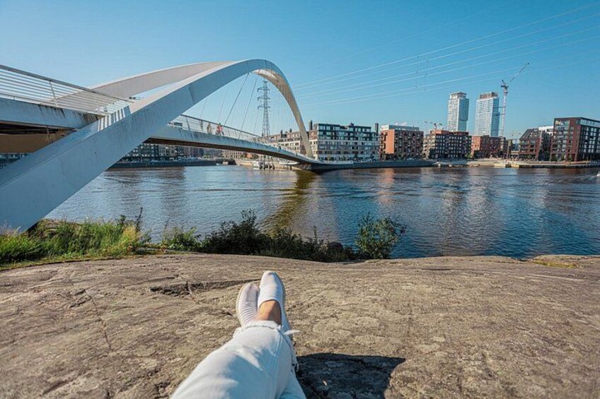 Un río con un puente moderno, edificios y una persona descansando sobre una roca. 2