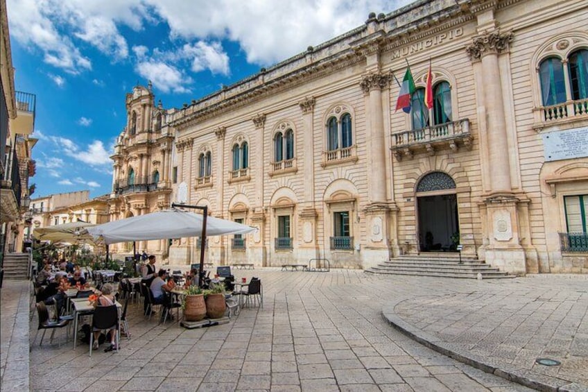 A historic building with flags, outdoor seating, and a cobblestone plaza. 2