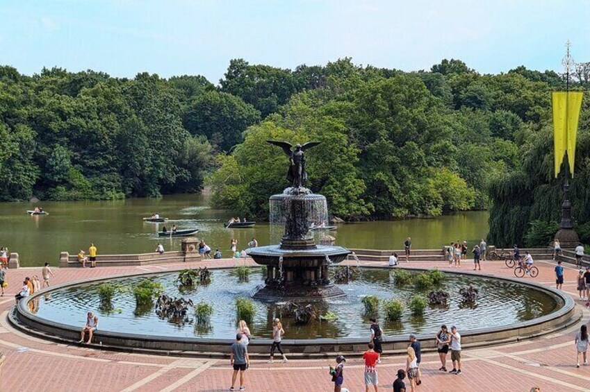 A park with a central fountain, a lake, and people walking around. 5