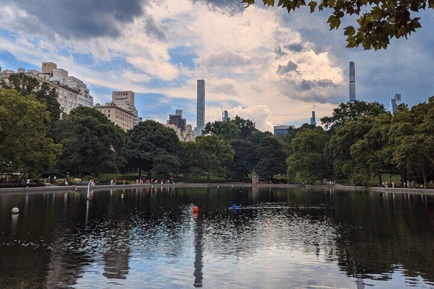 A park with a lake, trees, and buildings in the background. 4