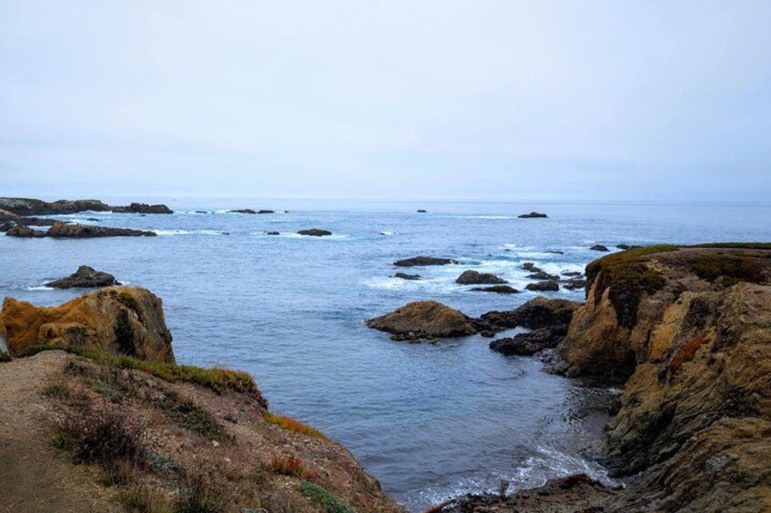 A coastal landscape with rocky cliffs, waves crashing against the shore, and a clear sky. 1