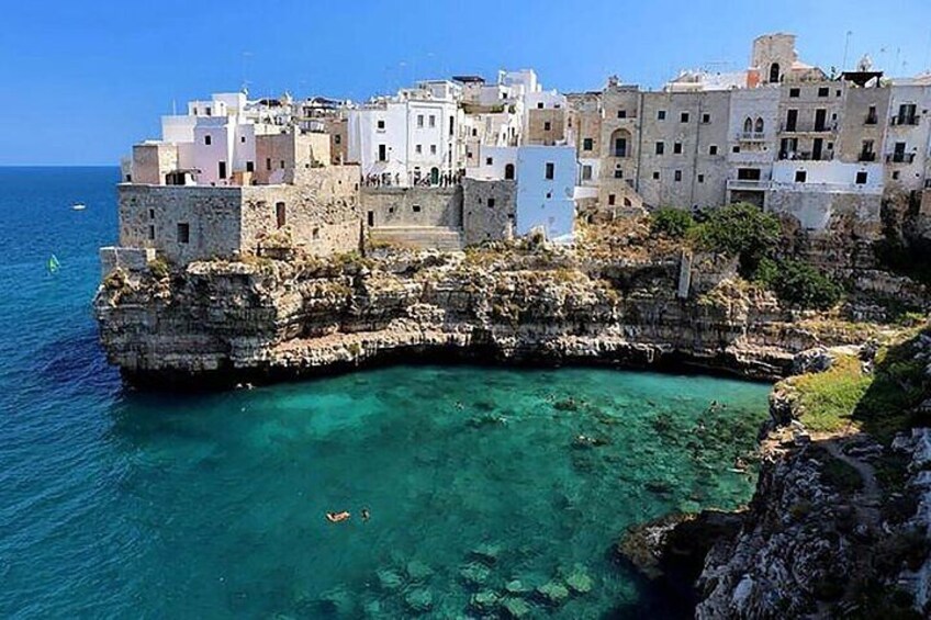 A coastal town built on a cliff, clear turquoise waters, and rocky terrain. 3