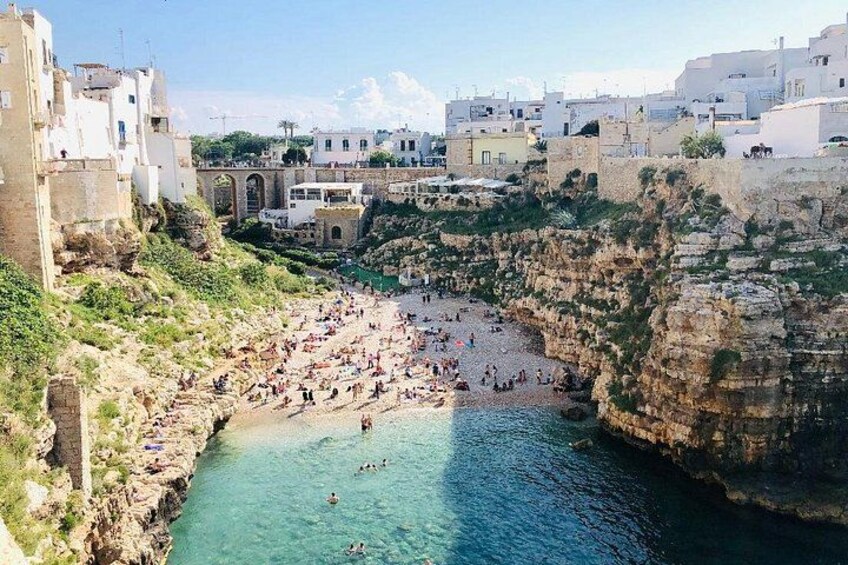 A coastal town with a rocky beach, clear blue waters, and historic buildings. 1