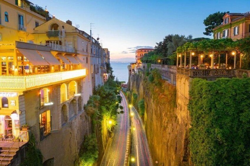 A coastal road with buildings on either side, a clear sky, and the sea in the distance. 5