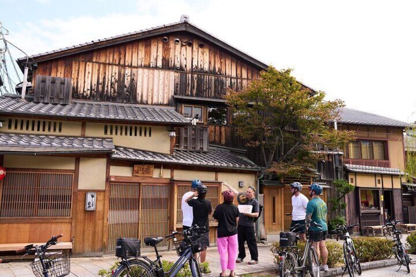 A traditional wooden building with a tiled roof, bicycles parked in front, and a group of people standing and conversing. 3