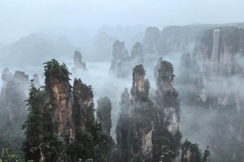 A misty landscape with towering limestone peaks and dense forestation. 4